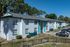 Charming suburban apartment complex with white stucco exterior and teal accents, surrounded by lush trees and ample parking space.