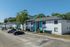 Charming apartment complex with white exteriors and turquoise accents, offering ample parking and lush greenery under a clear blue sky.