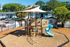 Charming outdoor playground with a modern play structure, vibrant slide, and shade sail, nestled in a lush residential area.