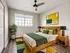 Bright and modern bedroom featuring a cozy wooden bed with colorful pillows, natural light streaming through large windows, and stylish decor, creating a welcoming and relaxing space.