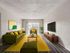 Inviting modern living room with chic green sofas, vibrant yellow accents, and a large window for natural light.