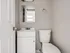 Modern bathroom with sleek fixtures, featuring a compact white vanity, a wall-mounted mirror, and a pristine toilet set against neutral walls.