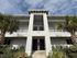 Modern apartment exterior with lush landscaping and palm trees, featuring a clean white facade and elegant balcony.