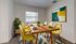 Bright and inviting dining room with modern wooden table, cheerful yellow chairs, vibrant artwork, and fresh decorations.