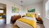 Inviting bedroom with modern furnishings, featuring a cozy bed with vibrant yellow and teal accents, elegant wooden furniture, and abstract art for a refreshing ambiance.