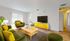 Bright and inviting living room with stylish green and yellow furnishings, featuring a cozy seating area, large TV, and modern decor.