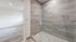Elegant bathroom featuring a modern glass shower with stylish gray tiles, opening to a bright room with sleek hardwood flooring.