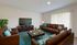 Inviting living room with elegant brown leather sofas, a sleek flat-screen TV, and a vibrant teal rug accented by floral pillows and fresh flowers.