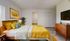 Bright and inviting bedroom with contemporary decor, featuring a cozy bed with vibrant yellow accents, stylish wooden furniture, and modern art on the wall.