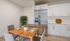 Modern kitchen and dining area featuring a sleek stainless steel refrigerator, elegant white cabinetry, and a stylish wooden dining table accented with greenery.