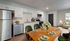 Contemporary open-concept kitchen and dining area featuring sleek white cabinetry, stainless steel appliances, and a stylish wooden dining table set for four with elegant green accents.