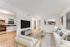 Modern open-concept living room with elegant furniture, wall art, and natural light flowing from large windows, seamlessly connected to a sleek kitchen.