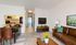 Bright and modern living space with a cozy leather sofa, vibrant yellow flowers, and a sleek TV setup. The open kitchen and dining area promise seamless entertaining.
