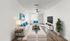 Bright and inviting living room with sleek modern decor, featuring white sofas, blue accent pillows, and a stylish coffee table. A flat-screen TV is mounted on the wall, complimented by elegant hardwood flooring and lush green plant for a touch of nature.