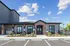 Charming clubhouse exterior with stylish brick facade, manicured landscaping, and ample parking under a clear blue sky.