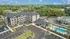 Aerial view of a modern apartment complex with a lush green backdrop, featuring a welcoming courtyard, ample parking, and a sparkling pool area.