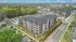 Bird's-eye view of a modern apartment complex featuring stylish architecture, lush greenery, ample parking, and a refreshing pool area, set in a vibrant neighborhood.