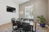 Modern conference room with sleek table, stylish chairs, and a flat-screen TV, featuring ample natural light and a serene view of a lush outdoor area.