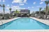 Elegant outdoor pool area with modern lounging furniture, surrounded by palm trees and a bright blue sky.