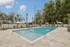 Luxury outdoor pool area with sleek sun loungers, umbrellas, and lush landscaping under a clear blue sky.