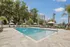 Inviting outdoor swimming pool area with chic lounge chairs and umbrellas set against a backdrop of lush greenery and blue skies.