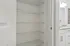 Pristine apartment showcasing a spacious white closet with elegant wire shelving adjacent to a modern bathroom with granite countertops.