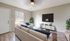Modern living room with elegant beige sofas, a large flat-screen TV, and stylish d&eacute;cor. Natural light filters through a window, complementing the contemporary aesthetic and green plant accents.