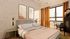 Elegant bedroom with modern decor, featuring artistic wall prints, natural light through large windows, and warm orange curtains.