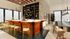 Elegant modern bar area with sleek wooden design, stylish bar stools, and a sophisticated liquor display, set in a bright, airy space with contemporary lighting and decor.