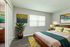 Bright and inviting bedroom with modern decor, featuring a cozy bed with colorful cushions, vibrant artwork, and a large potted plant for a touch of greenery.