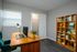 Modern home office with a sleek wooden desk, vibrant teal chair, and a stylish bookcase filled with books and decor.