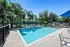 Inviting outdoor pool area with sun loungers and lush palm trees under a clear blue sky, offering a perfect relaxation spot.