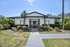 Charming white house with a welcoming entrance, surrounded by lush greenery and vibrant plants, under a clear blue sky.