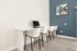 Modern and inviting workspace featuring a sleek desk with comfortable chairs and a computer setup, accented by a stylish abstract painting on a navy accent wall.