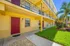 Charming apartment exterior featuring bright yellow walls, red doors, and vibrant landscaping with palm trees.