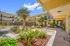 Charming apartment complex with vibrant landscaping, palm trees, and inviting walkways under a bright blue sky.
