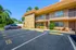 Charming two-story apartment building with a stone facade, surrounded by lush greenery and ample parking space, under a clear blue sky.
