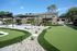 Charming outdoor area featuring a scenic putting green, elegant seating under shade sails, and lush palm trees for a relaxing atmosphere.