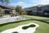 Inviting apartment courtyard with lush green mini-golf course, comfortable outdoor seating, and modern two-story buildings.