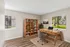 Bright, modern home office with large windows, wooden desk, and organized bookshelf, offering a serene view of lush greenery.
