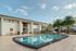 Inviting apartment complex with a pristine outdoor pool, surrounded by lush palm trees and spacious balconies under a clear blue sky.