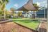 Inviting outdoor common area with modern shade sails, lush green lawn, and picnic tables amidst palm trees, perfect for relaxation and social gatherings.