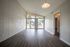 Bright and spacious living room with high ceilings and large windows, offering a view of the lush outdoors. Modern wood flooring enhances the inviting atmosphere.