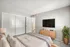 Inviting bedroom with plush bedding, modern TV setup, and stylish decor featuring a wooden dresser and lush green plant.