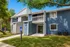 Charming blue apartment building with a welcoming porch and lush greenery, ideal for comfortable living.