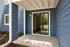 Inviting apartment entryway featuring elegant blue siding and a modern glass door opening to a serene garden view.