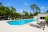 Inviting outdoor pool area with modern lounge chairs, surrounded by lush greenery and clear blue skies.