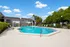 Inviting residential pool area with modern sun loungers and lush landscaping under a bright blue sky, perfect for relaxation and leisurely swims.