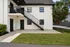 Charming duplex exterior with stylish black railings, lush landscaping, and a welcoming balcony perfect for relaxation.