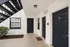 Modern apartment entrance with sleek black doors and a lush green shrub under an open staircase.